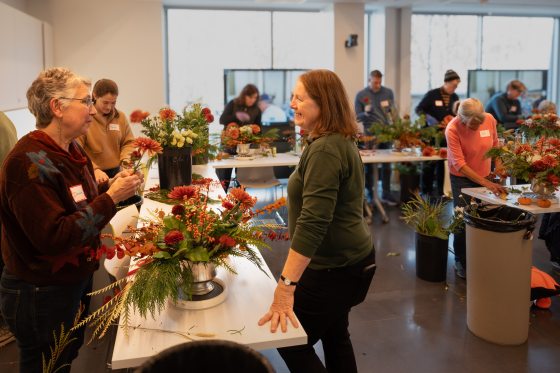 People standing at tables creating floral arrangements. 